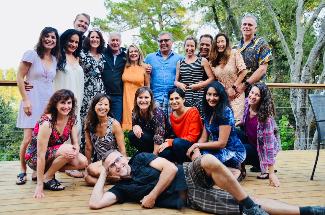 Claudia in a birthday tiara among a big group of smiling friends on a wooden deck under oak trees