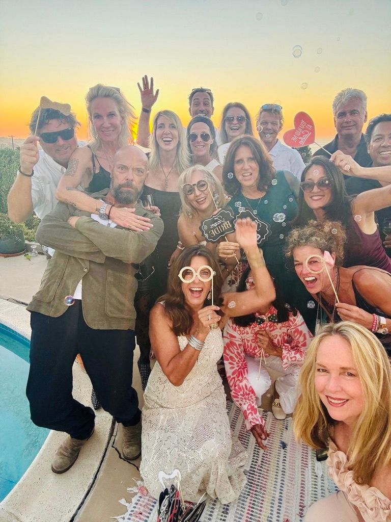 A crowd of friends laughing at a sunset party by a pool, a bride in a white lace dress in front, soap bubbles in the air