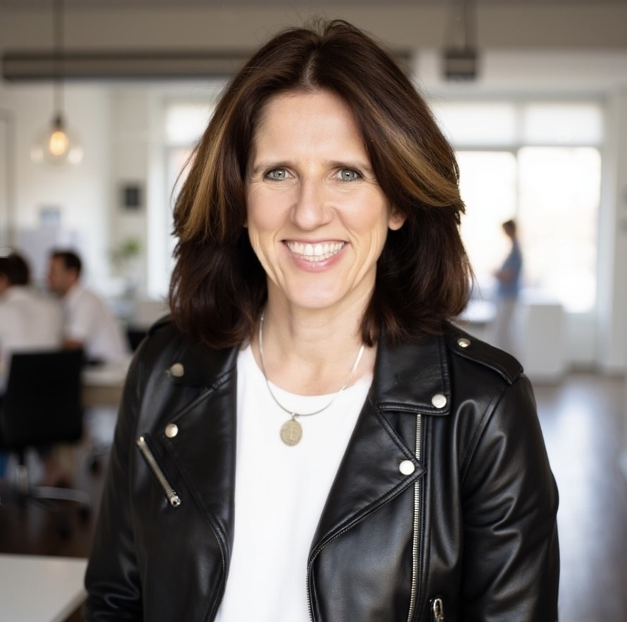Claudia Beck, MCC, founder of Better Together Group, smiling in a black leather jacket in a bright office
