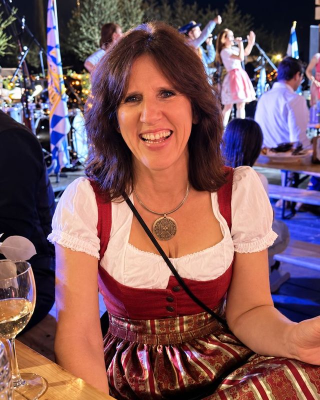 Claudia in a dirndl, laughing at a festival table at night