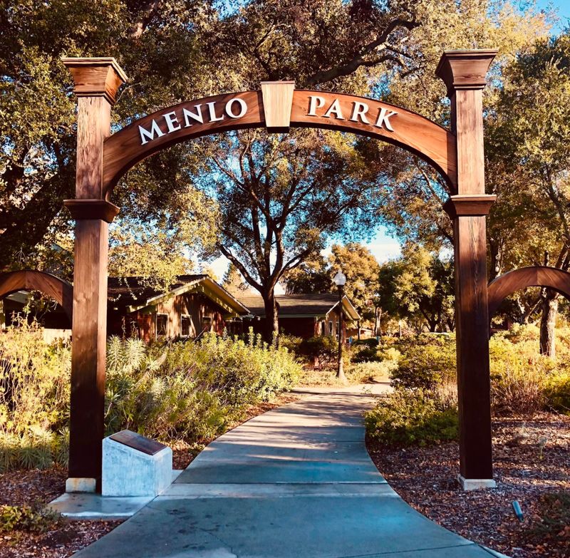 A wooden arch reading Menlo Park over a path lined with oak trees