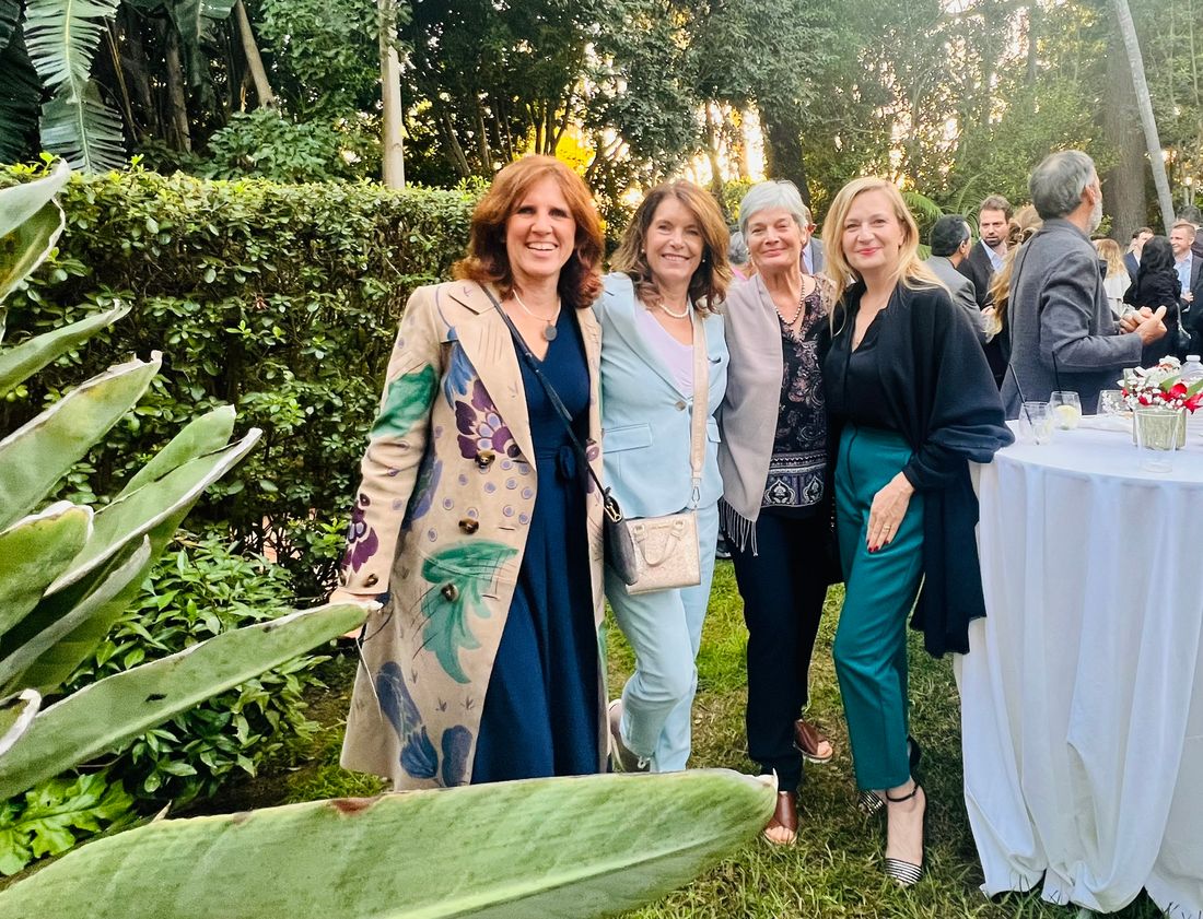 Claudia with three women at an evening garden reception, guests and a high table with red and white flowers behind them