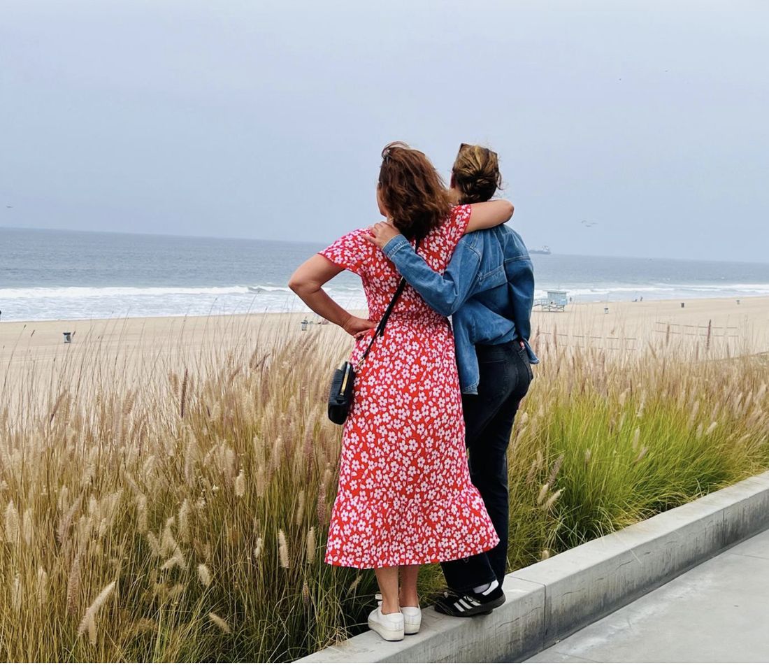 Claudia and her niece from behind, arm in arm, looking out over beach grass to the ocean
