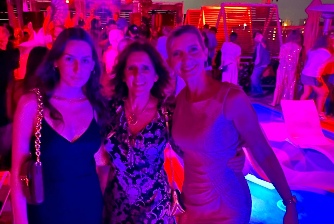 Claudia between her niece and another woman at a rooftop party at night, lit in pink and purple