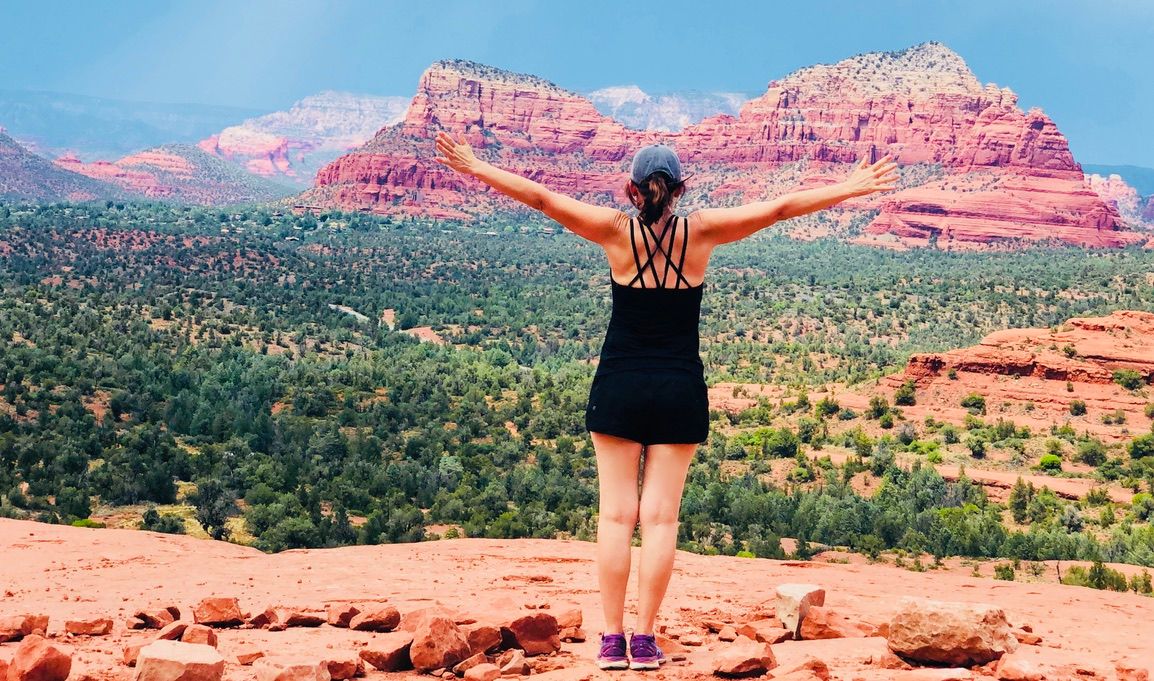 Claudia from behind with her arms stretched wide, facing the red rocks of Sedona