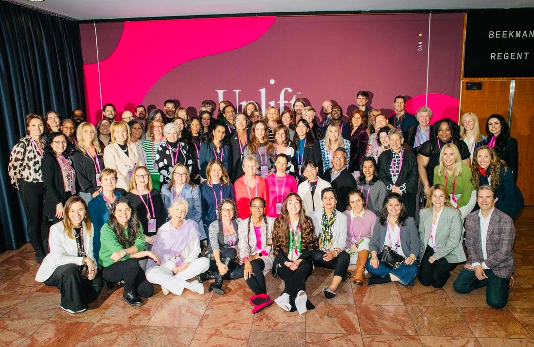 A large group of conference attendees with lanyards posing in front of an Uplift backdrop in New York