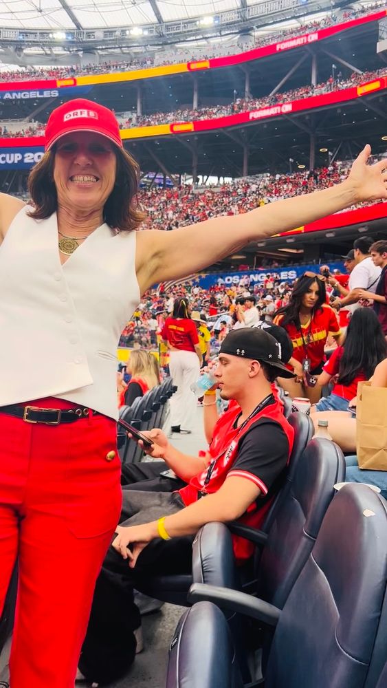 Claudia with her arms spread wide in a red cap at a World Cup match